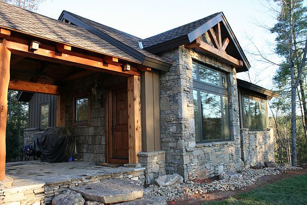 House plan exterior showing stone facade, wood porch with exposed beams, gable detail, and shingle siding.