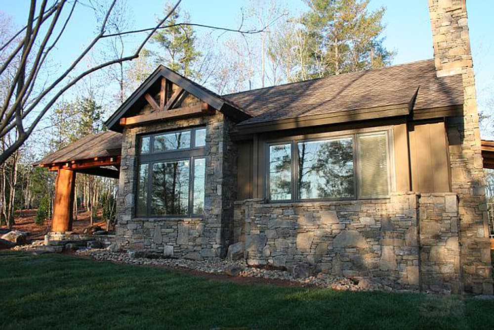 House plan exterior: Modern rustic style with stone facade, large windows, and exposed timber roof structure.
