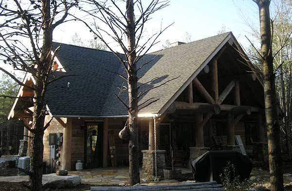 Log cabin exterior with exposed timber framing, a steep gable roof, and a covered porch supported by stone columns.