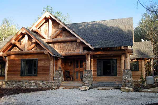 Log home exterior with prominent timber framing, stone accents, gabled dormers, and a covered porch.