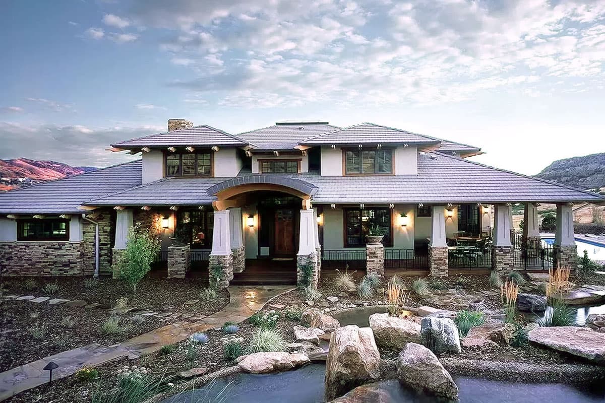 House plan exterior: Craftsman style, two stories, wide eaves, stone accents, covered porch with stone columns, multiple gables.