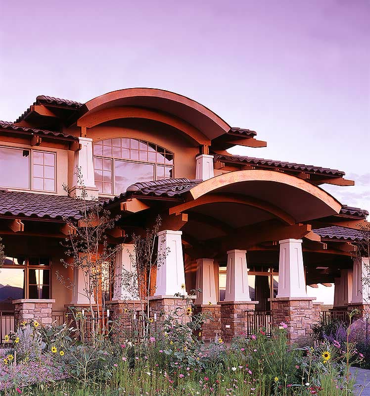 House plan exterior features arched rooflines, stone-clad pillars, and a prominent entryway with timber accents.