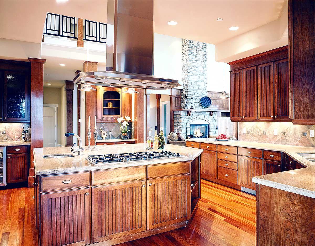 Kitchen with large island, stone fireplace, and wood cabinetry. Elevated walkway with railing visible in background.