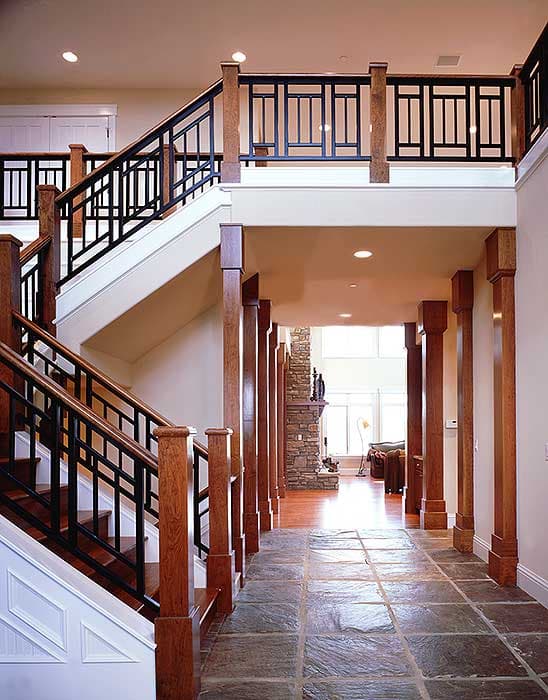Interior view of a multi-level house foyer with a U-shaped staircase, wood newel posts, black metal railings, and stone flooring.