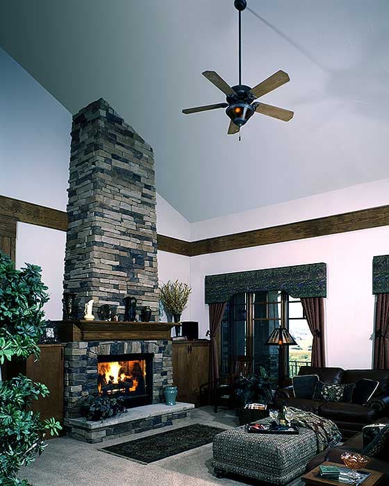 Great room interior rendering featuring a floor-to-ceiling stone fireplace, vaulted ceiling with exposed beams, and a ceiling fan.