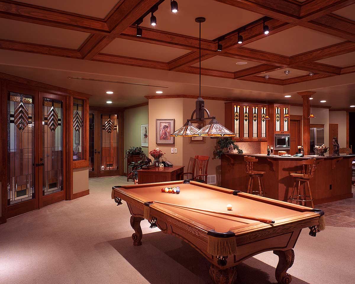 Interior view of a basement rec room with pool table, wet bar with wood cabinetry, and stained glass doors.