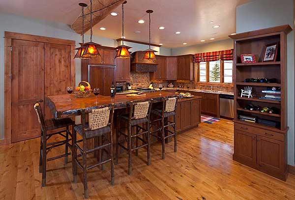 Rustic kitchen with live-edge island, wood cabinetry, pendant lights, and built-in bookshelf.