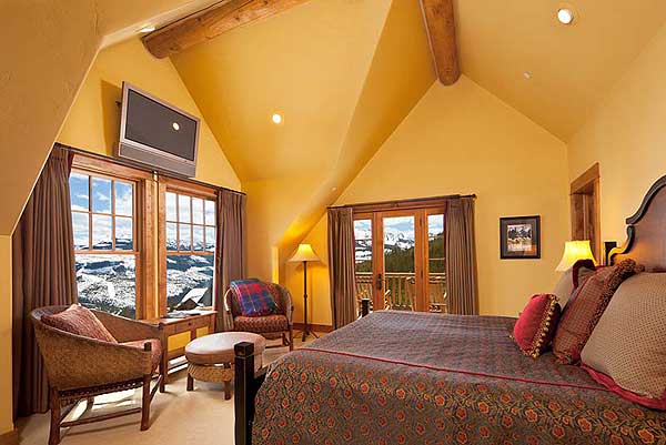 Bedroom with vaulted ceiling, exposed beams, mountain views through French doors and double-hung windows.
