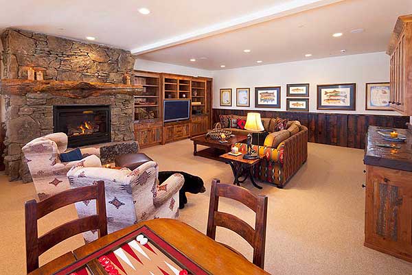 Interior living area with stone fireplace, built-in bookshelves, sofa, and chairs. Rustic wood accents and fish artwork visible.