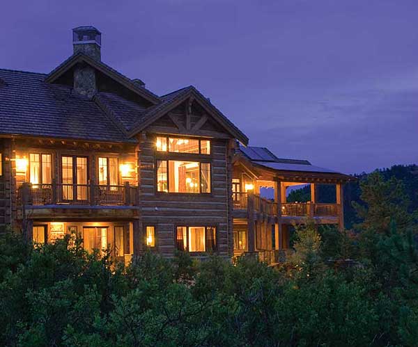 Log home exterior with multiple stories, large windows, balconies, and a covered porch with solar panels.