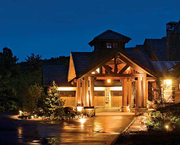 House plan exterior: Rustic lodge style with covered porte-cochère, exposed timber framing, multiple gables, and a multi-story structure.