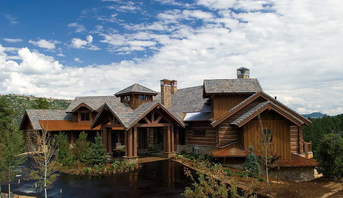 Log home exterior with multi-level roofs, stone chimney, exposed timber framing, and a covered entryway.