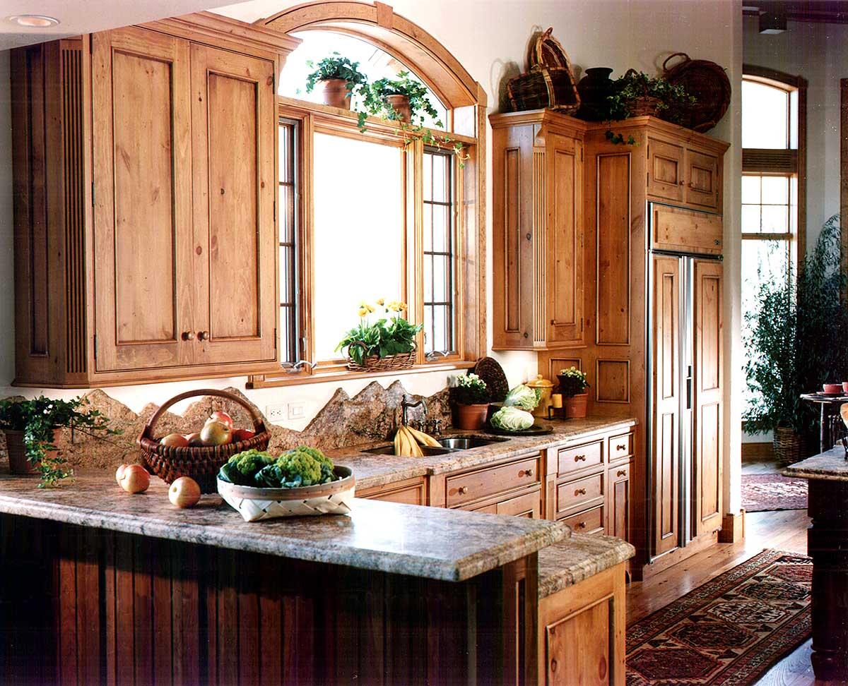 Kitchen interior with knotty pine cabinets, granite countertops, arched window, and stainless steel refrigerator.