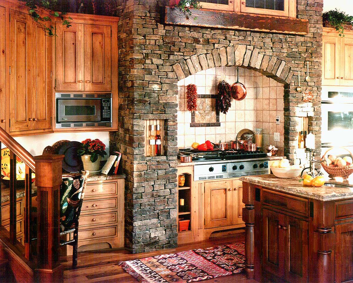 Country kitchen with stone archway over stove, wooden cabinetry, and island.