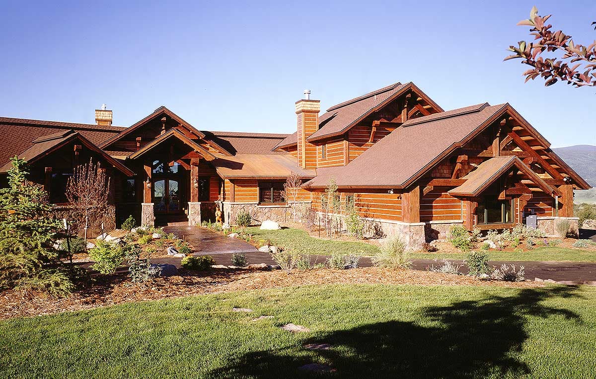 Log house plan exterior featuring prominent gables, timber framing, stone accents, and a covered entry with large windows.