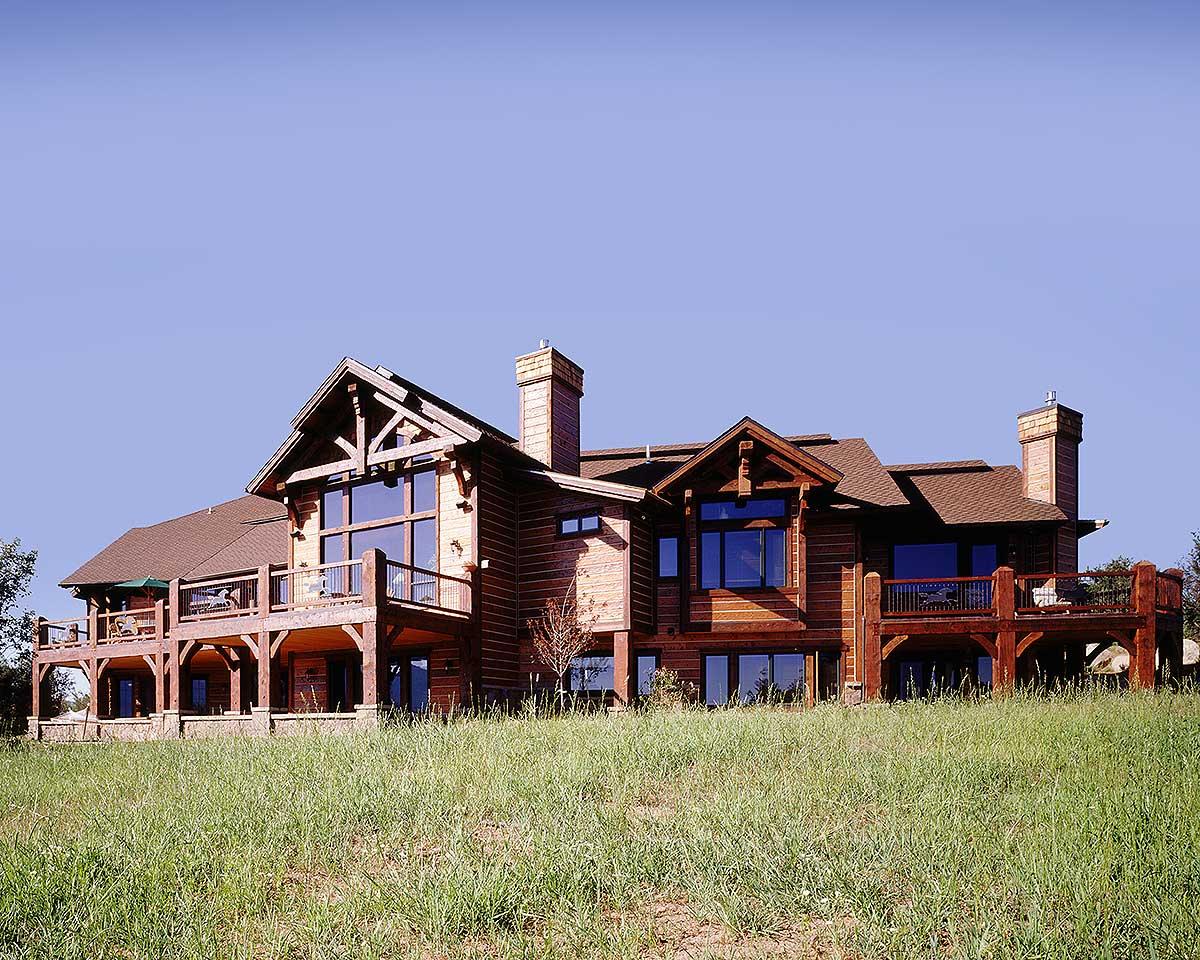 Log home exterior with multiple stories, large windows, exposed beams, wrap-around decks, and prominent chimneys.