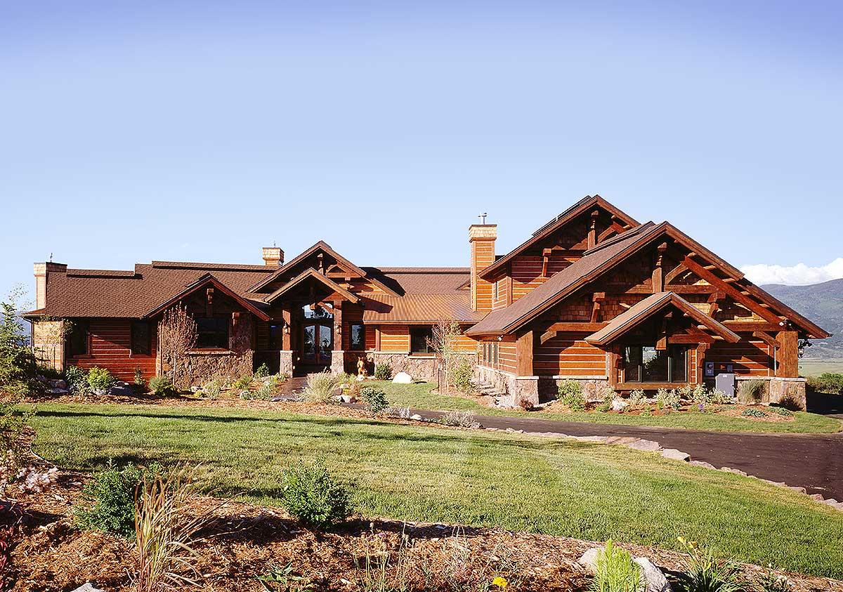 Log home exterior with exposed timber framing, stone accents, and multiple gables. House plan is one story.