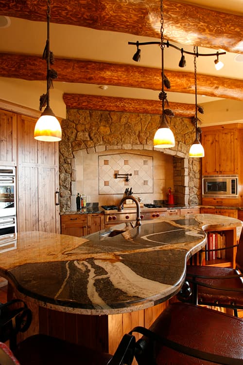 Kitchen with stone arch range hood, wood cabinetry, granite island, and log beam ceiling.
