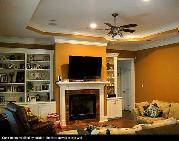 Great Room interior view with built-in bookshelves, fireplace, entertainment center, tray ceiling, and ceiling fan.