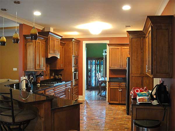 Kitchen with wood cabinetry, granite countertops, gas range, pendant lights, and brick flooring.