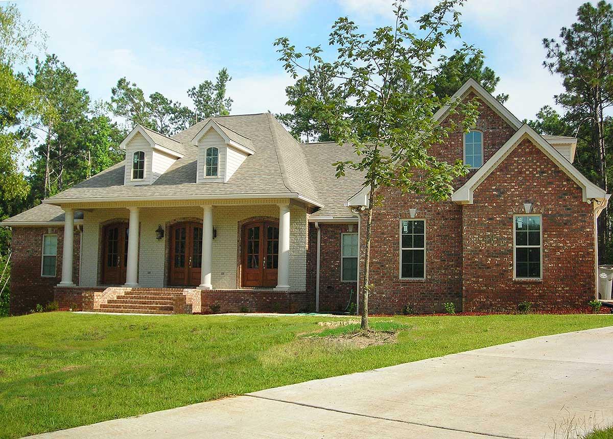 House plan exterior: Brick and white siding two-story home with a covered porch supported by columns, dormers, and a gabled roof.