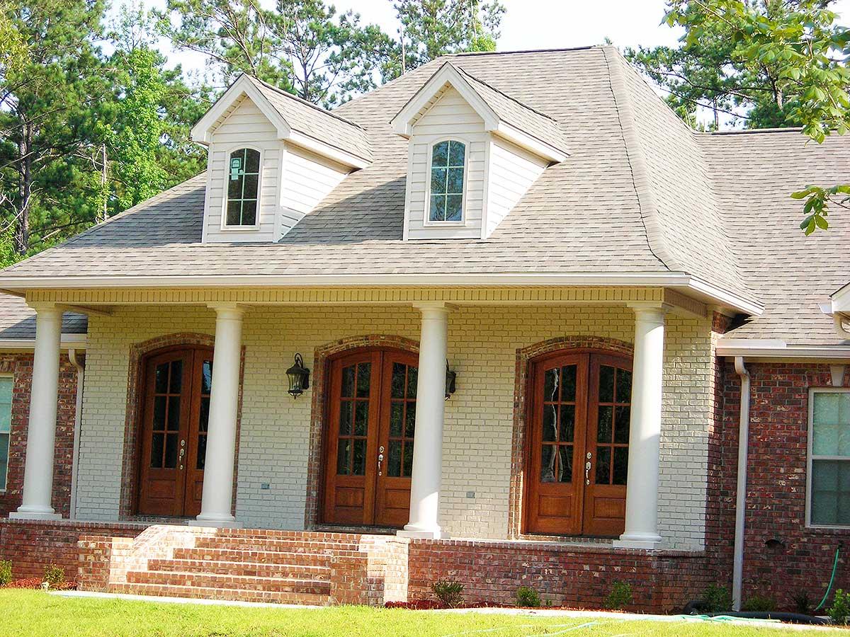 House plan exterior featuring a covered porch with three sets of double doors, white columns, dormers, and brick and white siding.
