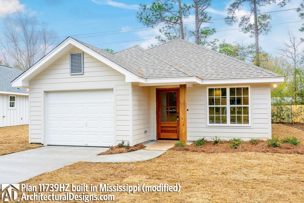 House plan exterior: One-story home with a front-facing garage, gable vents, and a wood-paneled front door.