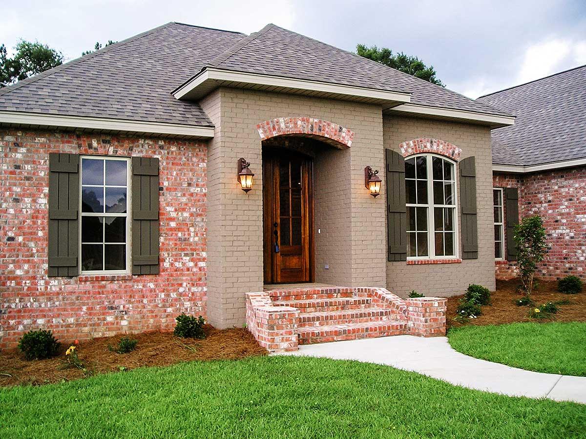 House plan exterior: one-story home with brick facade, arched entryway, brick steps, and dark shutters.