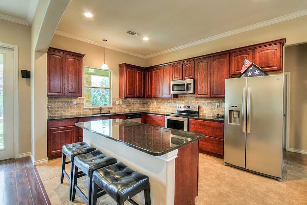 Kitchen with dark wood cabinets, granite-topped island with bar seating, stainless steel appliances, and tile backsplash.