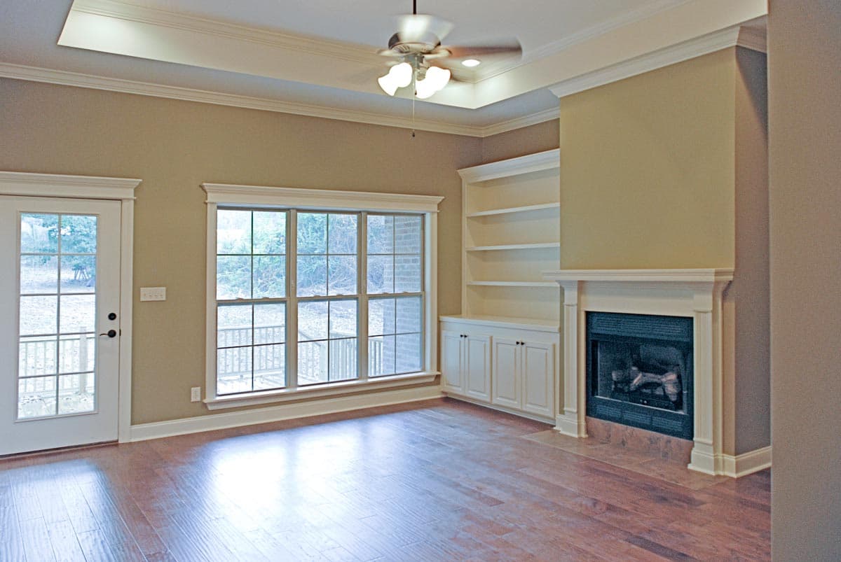 Living room with fireplace, built-in shelving, ceiling fan, and French doors leading outside.