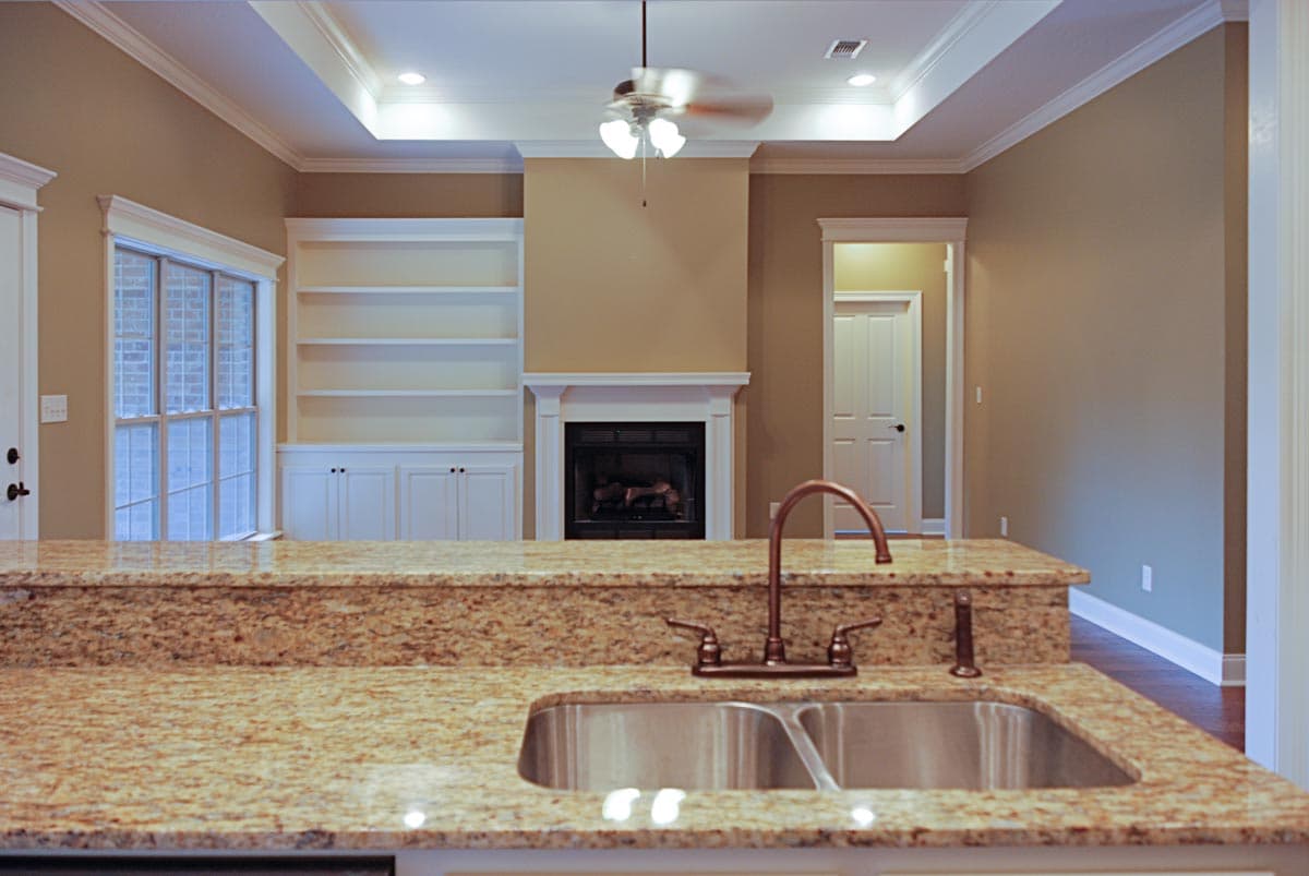 Kitchen with granite countertop, stainless steel sink, fireplace with built-in shelves, and a tray ceiling with fan.