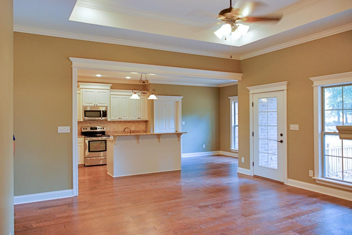 Interior rendering of an open-concept living area connecting to a kitchen with a breakfast bar, stainless steel appliances, and white cabinetry.