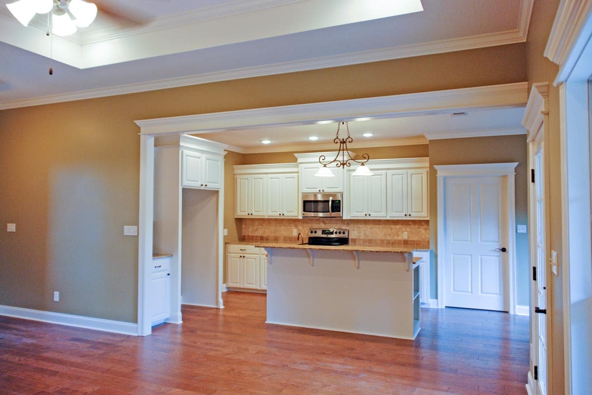 Interior view of a kitchen with white cabinets, island, and stainless steel appliances. Tray ceiling and hardwood floors visible.