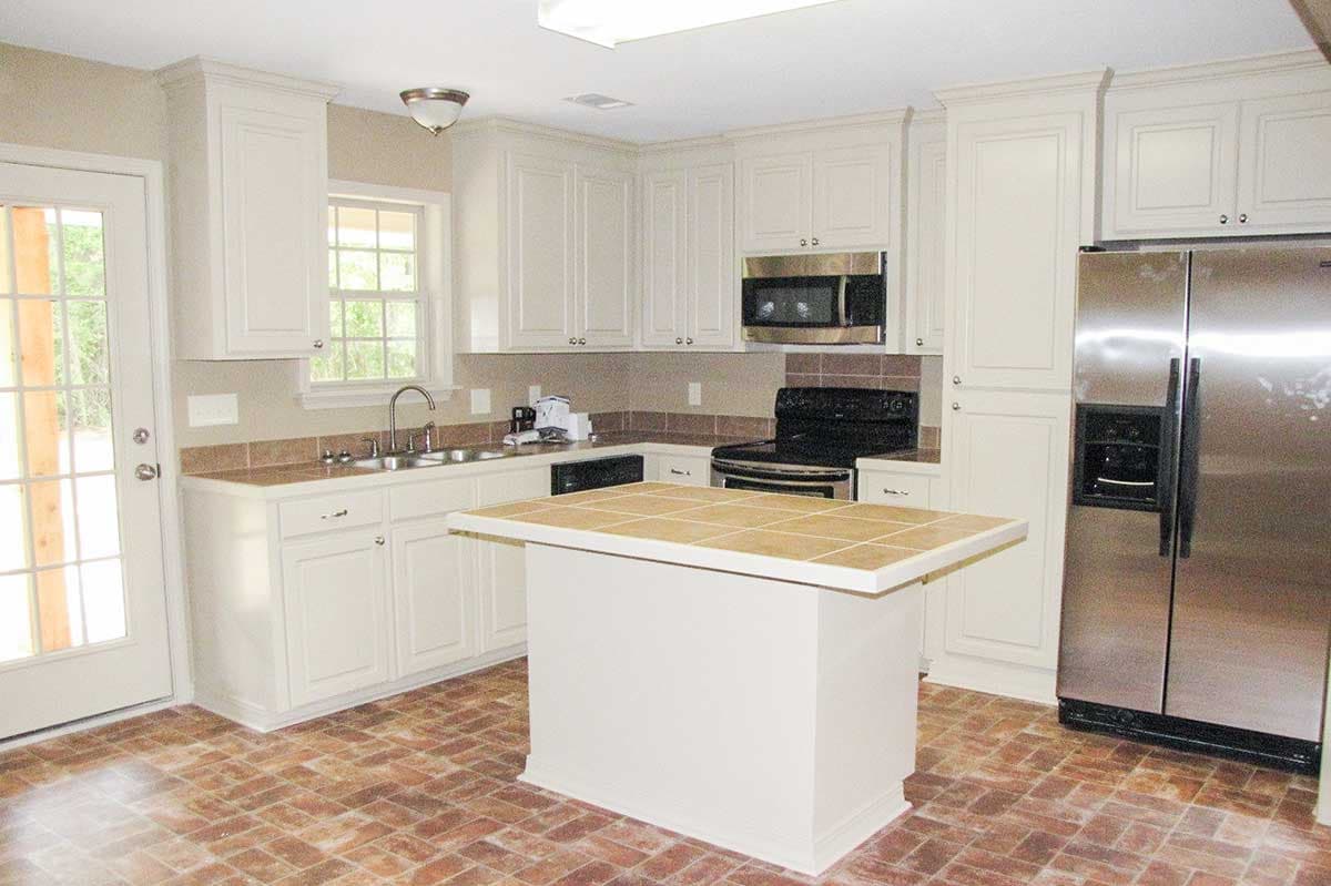 Kitchen with white cabinets, a central island with tiled countertop, stainless steel refrigerator, and brick-patterned flooring.