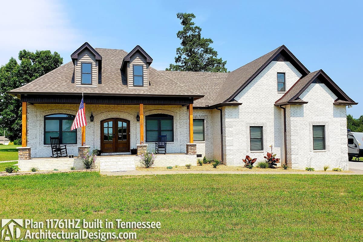 House plan exterior of a two-story modern farmhouse with a covered front porch supported by wooden posts and a gabled dormer.