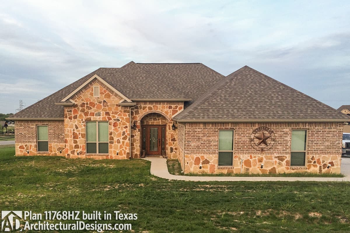 One-story house plan exterior with arched brick entryway, stone accents, and multi-level gabled rooflines.