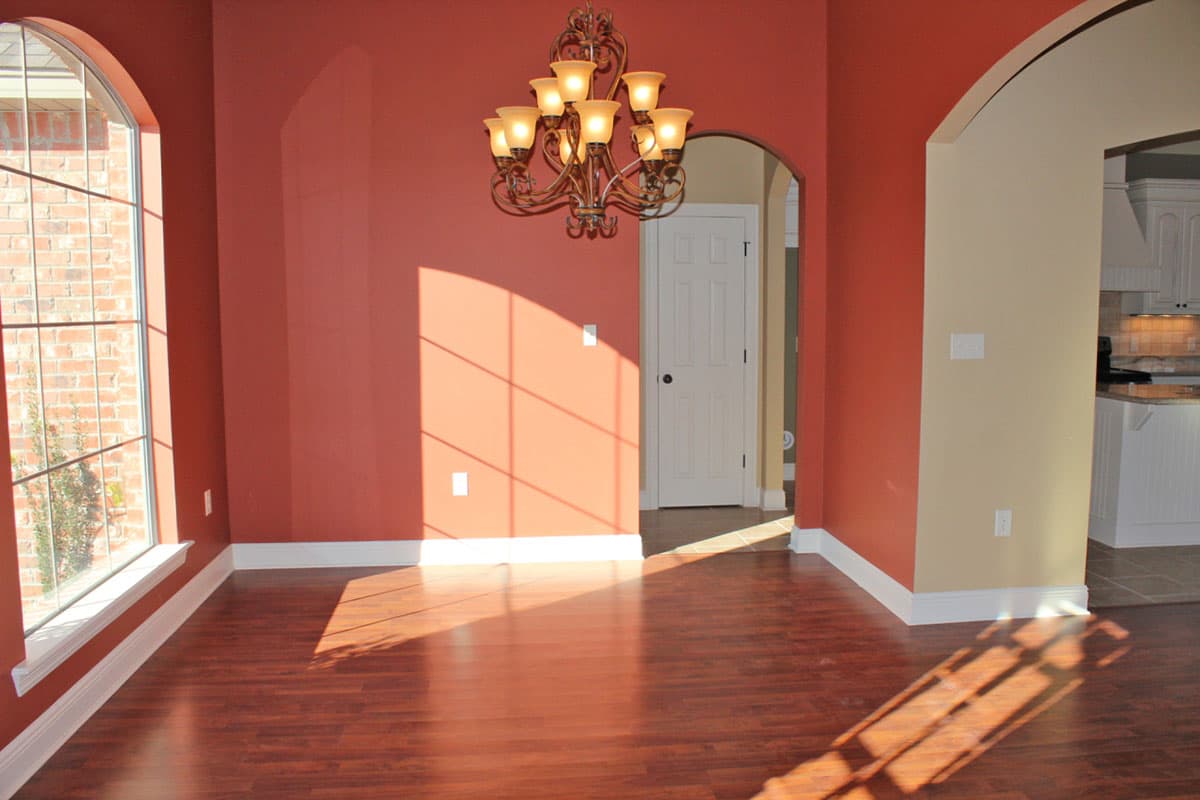 Interior view of a house with archways, a chandelier, and a large arched window. A kitchen is visible through an opening.