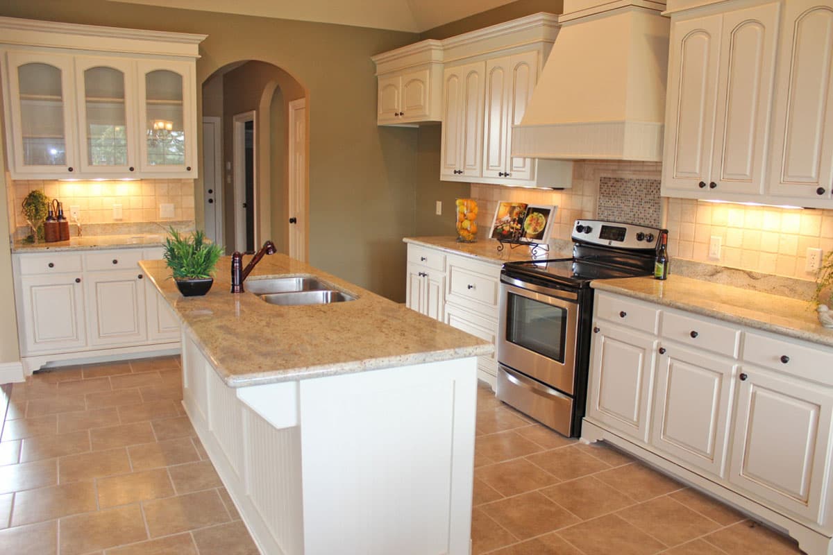 Kitchen interior with white cabinets, granite countertops, a large island with sink, and stainless steel range.