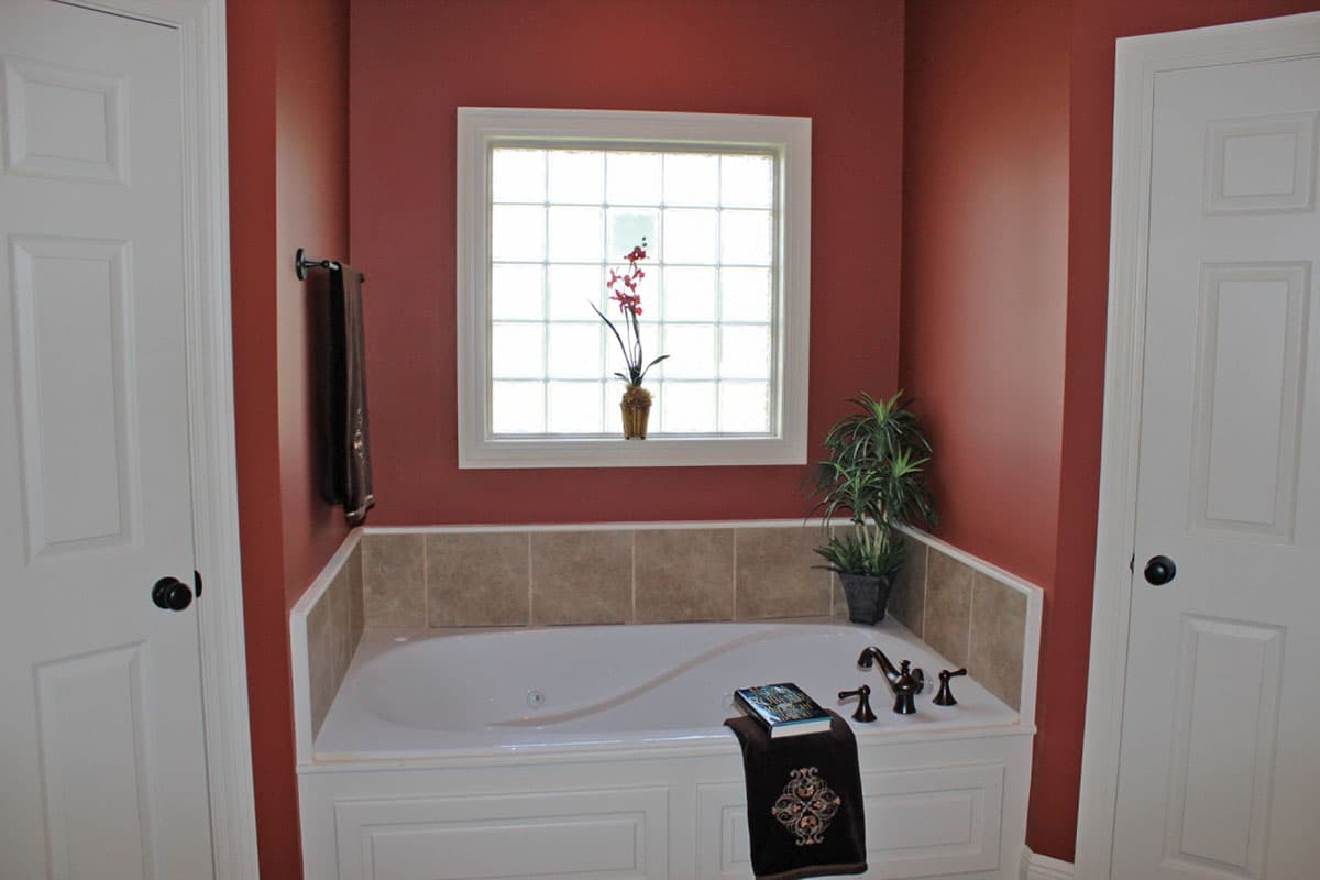 Bathroom with jetted tub under a grid window, flanked by white doors and accented by potted plants.
