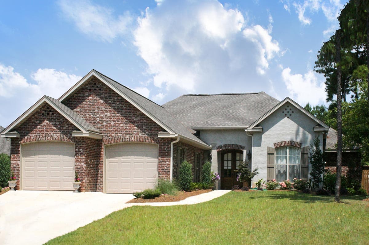 House plan exterior: One-story home with brick and stucco, a three-car garage, arched entry, and gabled dormers.