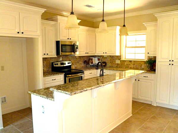 Kitchen with white cabinets, granite countertops, island with seating, stainless steel appliances, and pendant lighting.