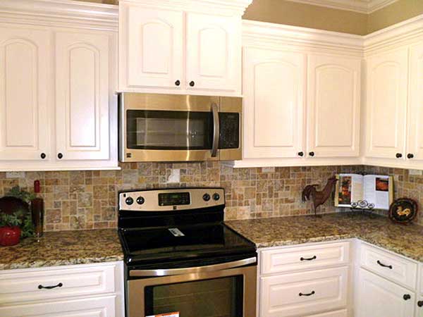 Kitchen interior with white cabinets, stainless steel microwave and range, granite countertops, and mosaic tile backsplash.