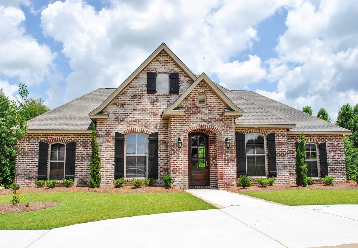 House plan exterior: one-story brick home with arched entryway, multiple gables, dormer window, and black shutters.