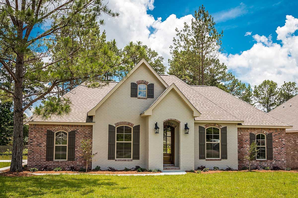 House plan exterior featuring a one-story, brick and stucco facade, arched entryway, gables, and shuttered windows.
