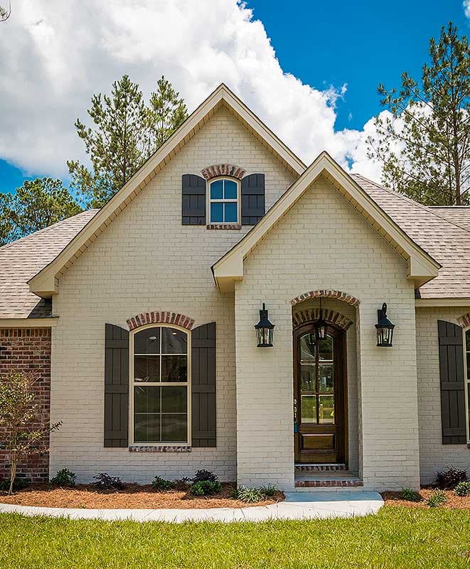 House plan exterior: Traditional style home with arched entry, brick accents, dormer window, and shutters.