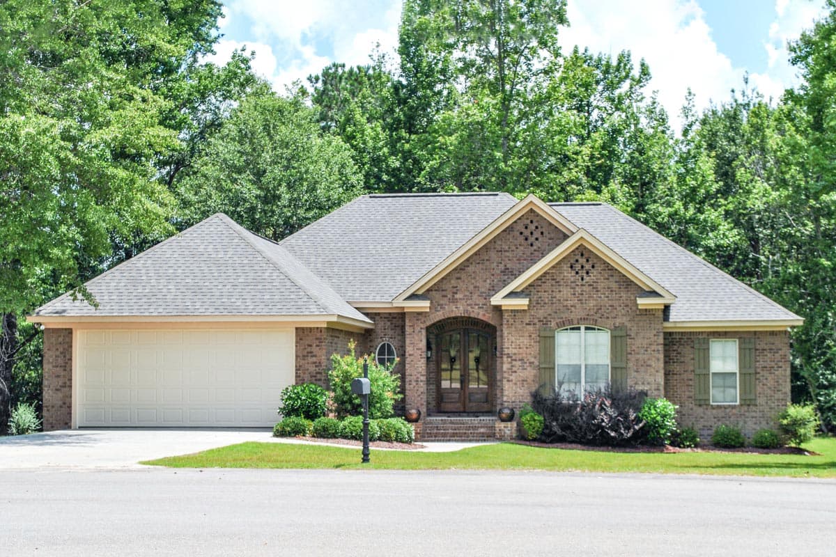 House plan exterior: One-story brick home with attached garage, arched entryway, and multiple gables.