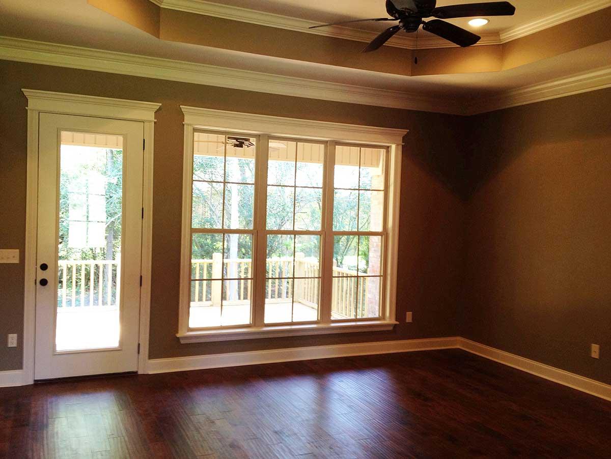 Interior view of a room with a tray ceiling, ceiling fan, French door, and large picture window overlooking a deck.