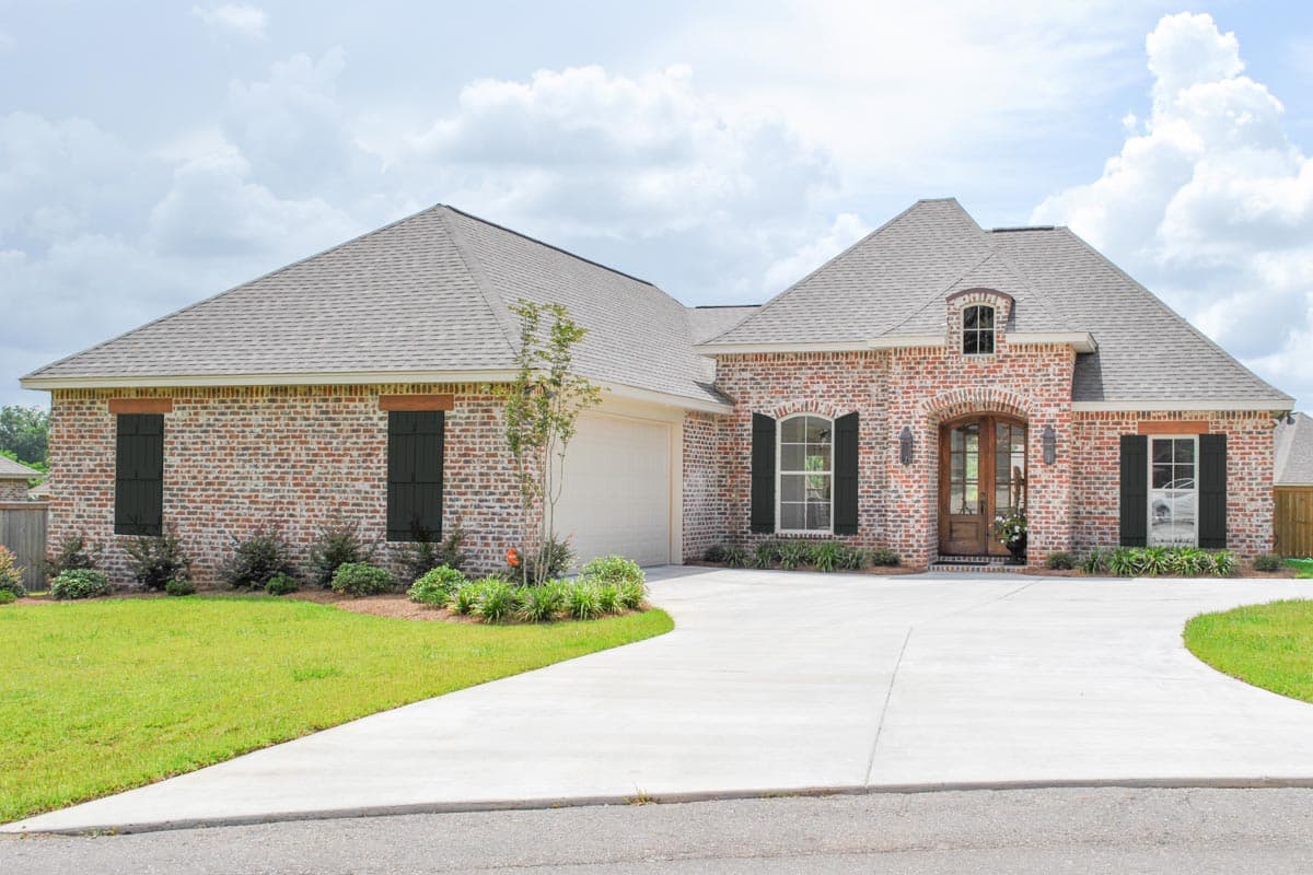 House plan exterior: Single-story brick home with a prominent arched entryway, dormer window, and attached garage.