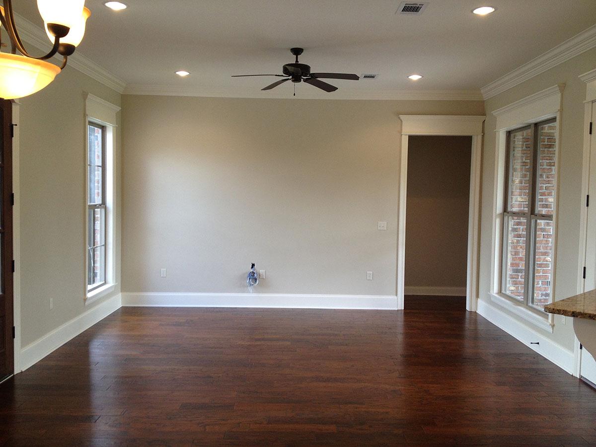 Interior view of an open-concept living space with dark hardwood floors, two tall windows, crown molding, and a ceiling fan.