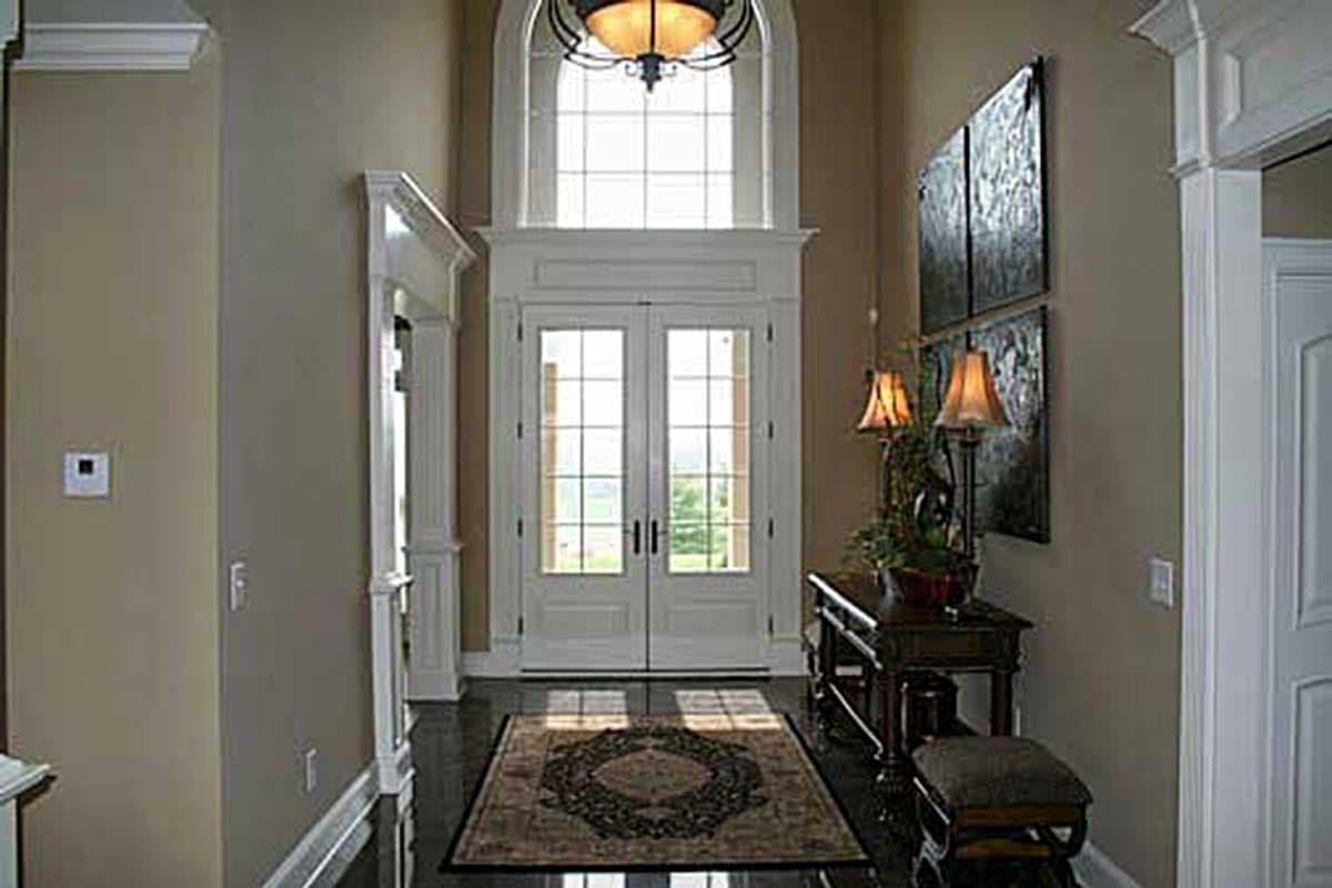 Interior view of a foyer with double glass doors, arched transom window, dark hardwood floors, and decorative rug.